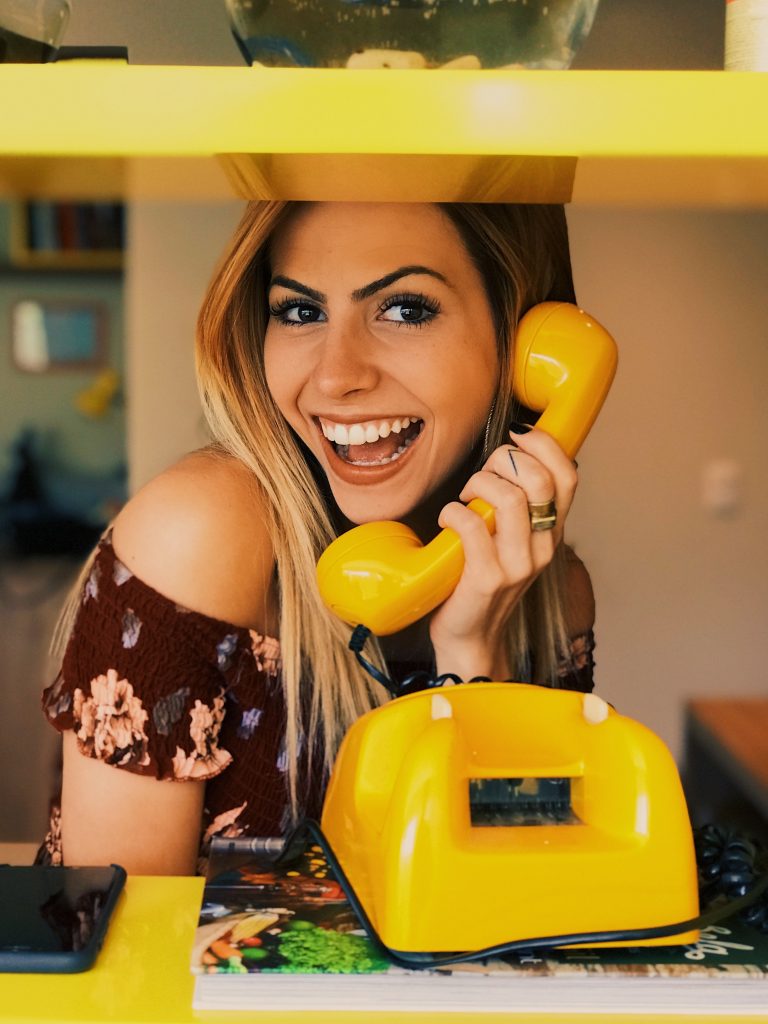 Woman holding yellow rotary telephone with smile
