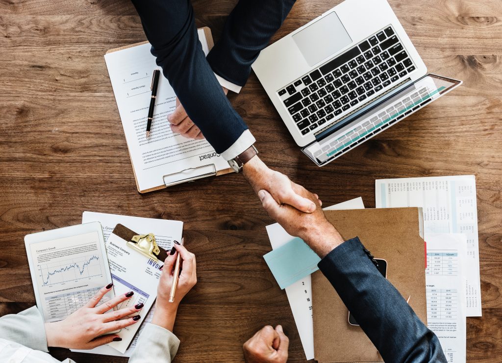 two people handshaking above table with laptop